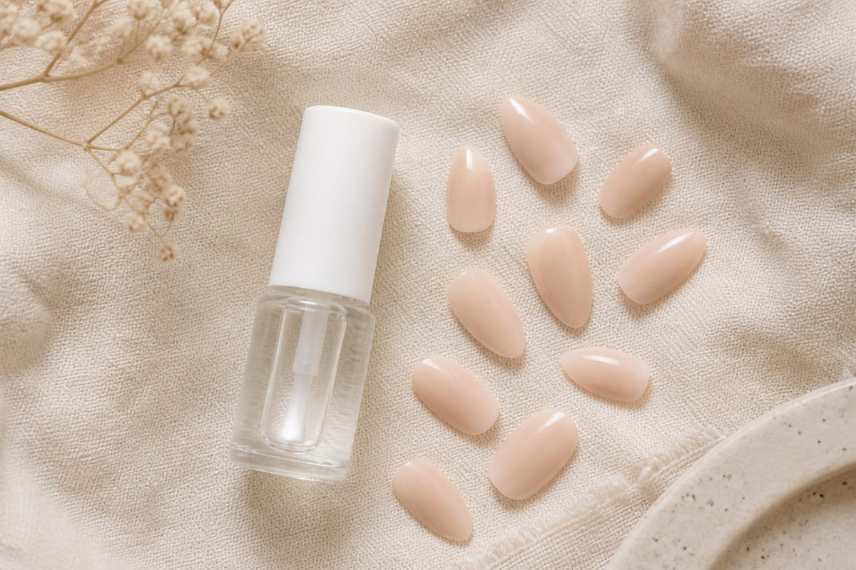 Brush-on nail glue bottle beside soft almond press-on nails and a wooden stick